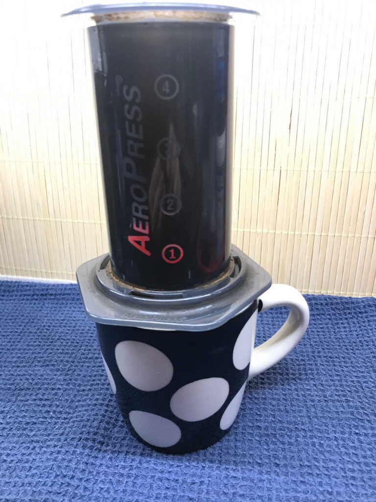 A plunged AeroPress standing on a black and white polka dot mug