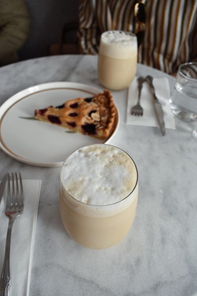 Two butterscotch lattes in glasses with foamed milk and a drizzle of butterscotch syrup on top. There is also a lslice of cherry lattice pie on a plate.