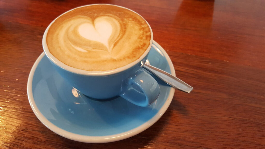 Flat white coffee with heart shape coffee art on the surface in a blue cup and saucer standing on a wooden table