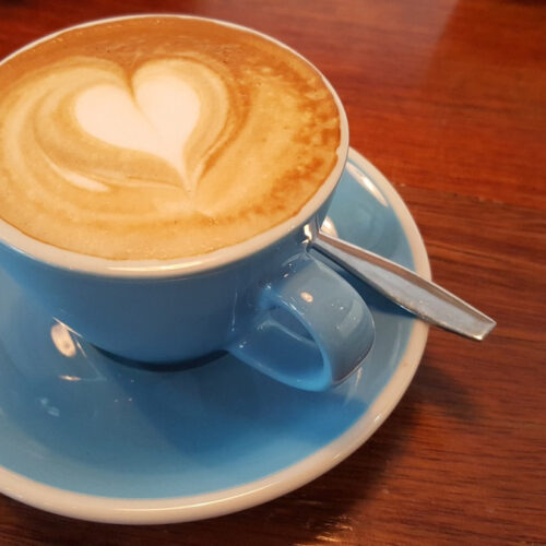 Flat white coffee with heart shape coffee art on the surface in a blue cup and saucer standing on a wooden table