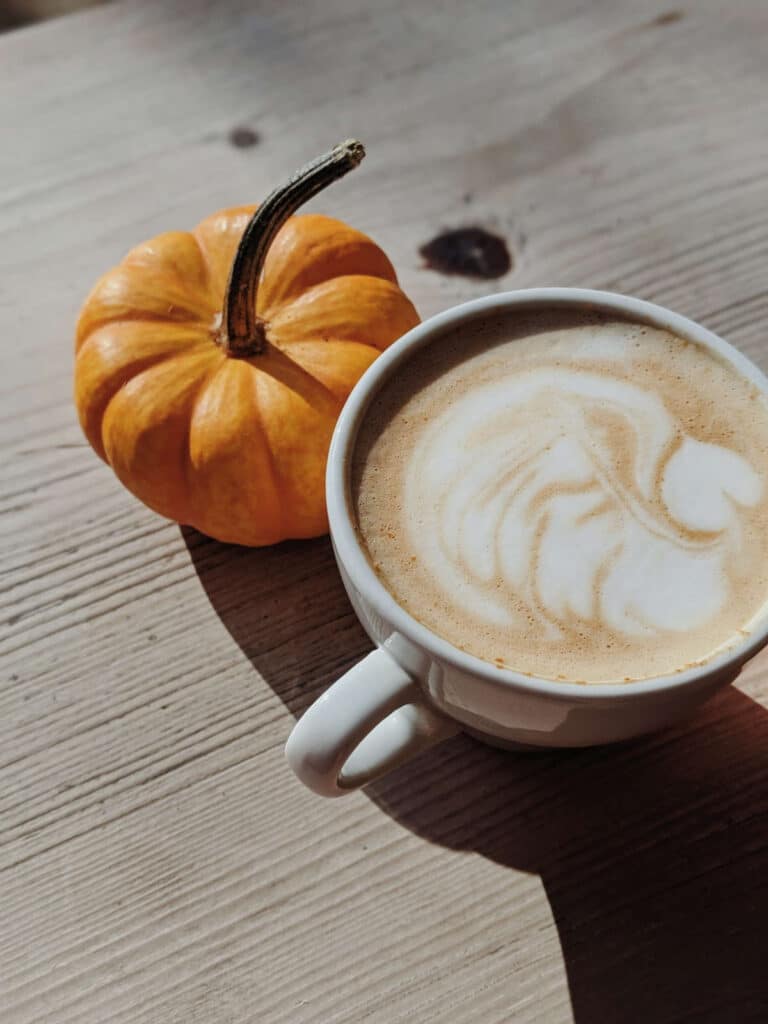 a cup of pumpkin spice latte standing on a wood table with a miniature pumpkin behind