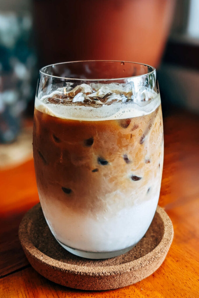A glass of iced caramel latte standing on a cork coaster on a wooden table