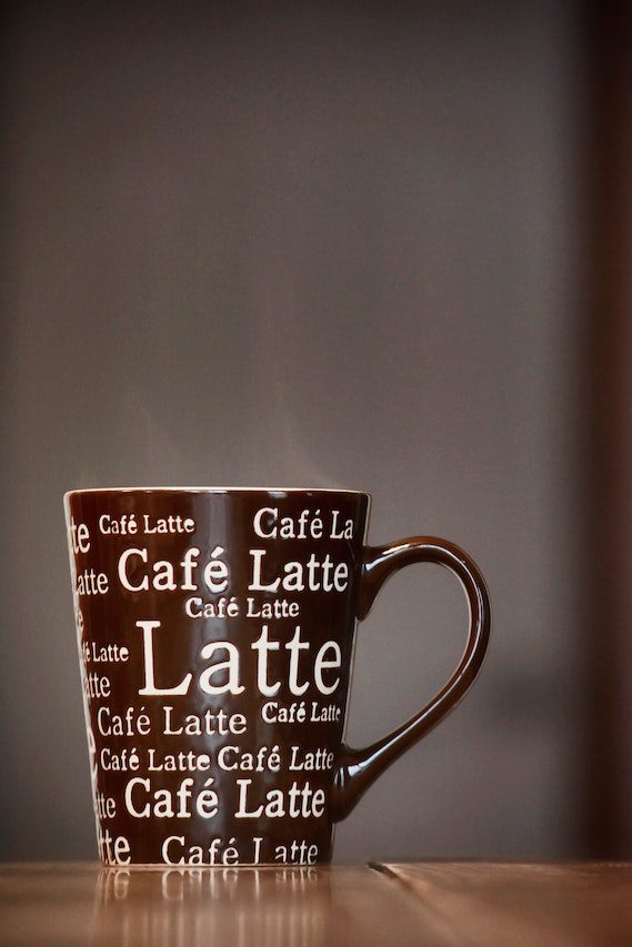 Brown mug with the word latte written all over standing on a wooden table.