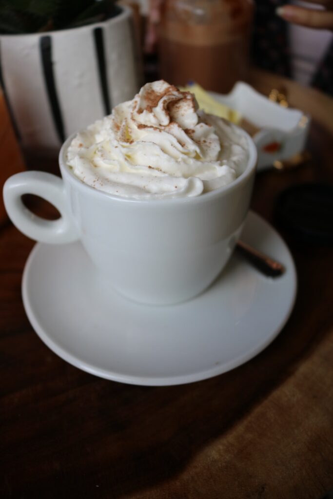 a white chocolate latte with whipped cream and chocolate powder on top, standing on a wooden talbe.