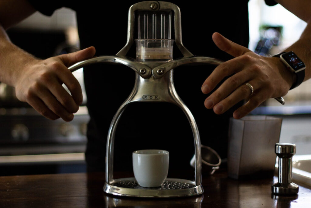 A man pushing down the two levers of a manual espresso maker to brew a shot of espresso
