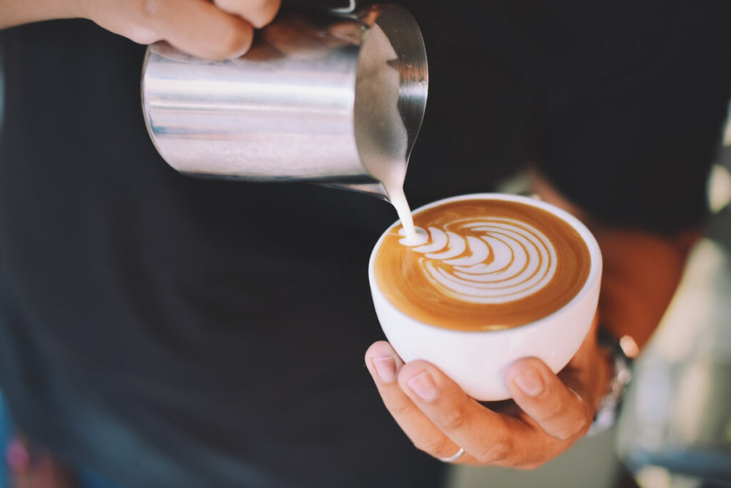 Barista pouring foamed oat milk into a cup of latte