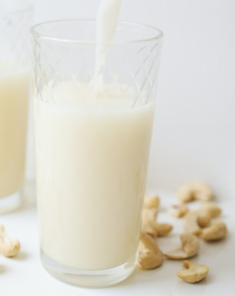 Pouring a fresh glass of cashew milk. With whole cashew nuts scattered around.