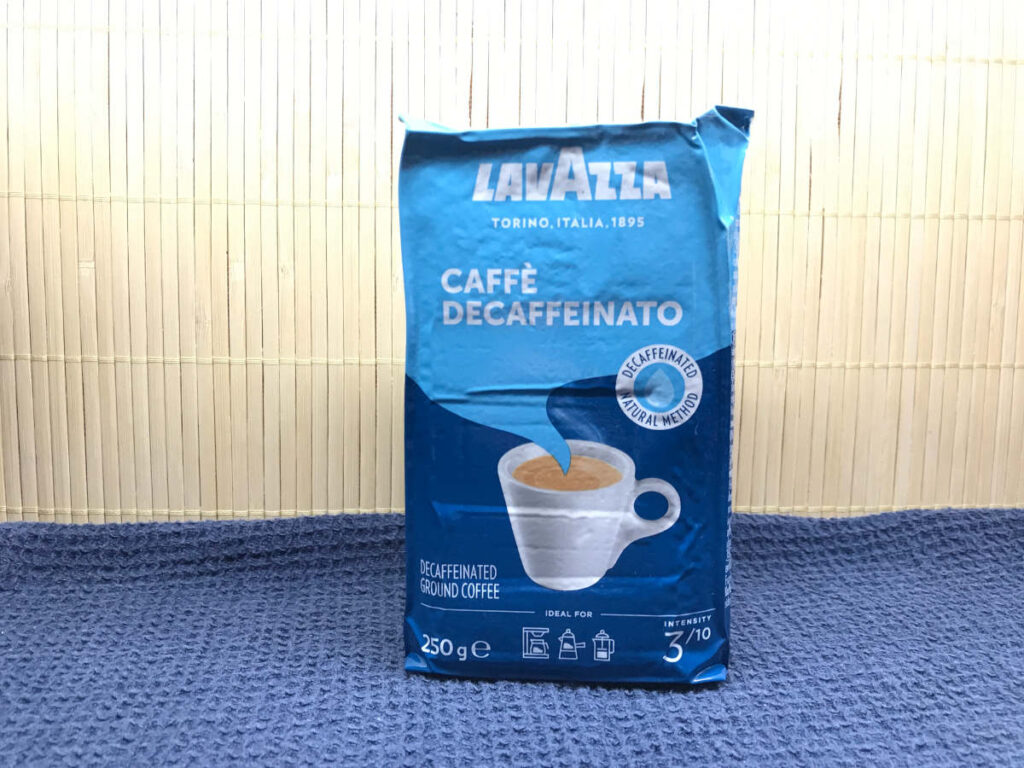 An unopened pack of pre-ground Lavazza decaffeinated coffee on a blue surface.