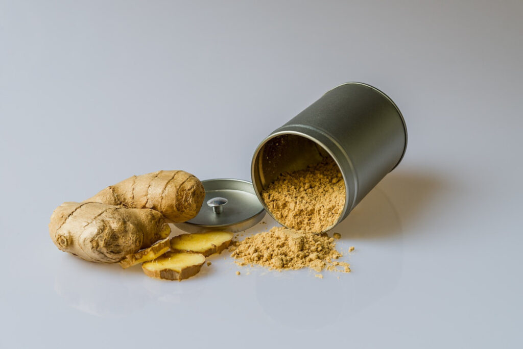 Chopped piece of fresh ginger next to a spilled jar of ground ginger.