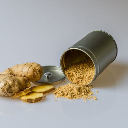 Chopped piece of fresh ginger next to a spilled jar of ground ginger.