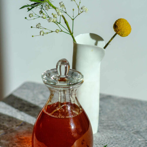 Salted caramel syrup in a clear bottle standing in front of a vase with dried flowers.