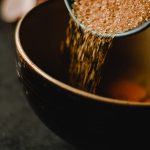 Pouring a bowl of demerara brown sugar into a saucepan to make syrup.
