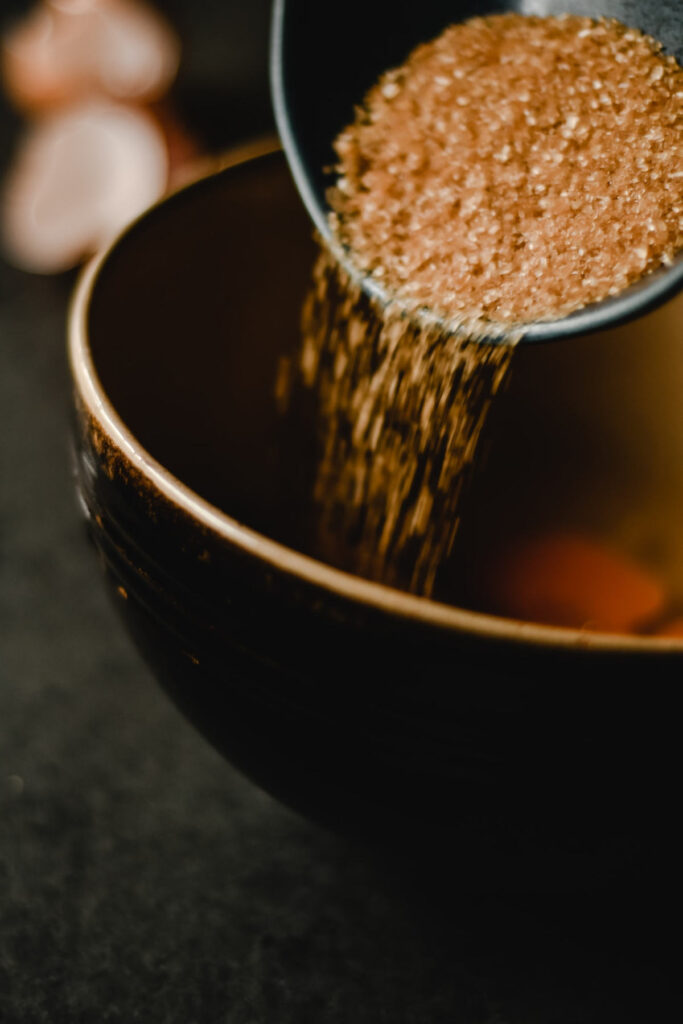 Pouring a bowl of demerara brown sugar into a saucepan to make syrup.