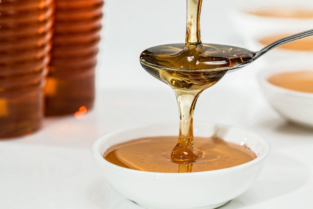 Pouring caramel syrup over a spoon into a white bowl.