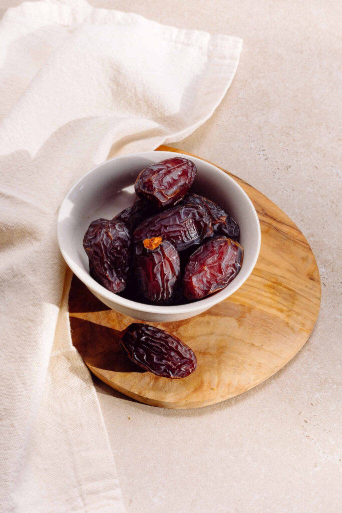 A bowl of dates standing on a wood plate.