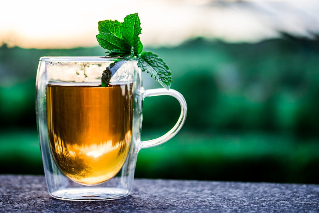 A glass cup of peppermint syrup with a few peppermint leaves resting on the top.