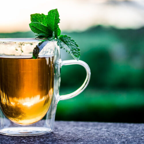 A glass cup of peppermint syrup with a few peppermint leaves resting on the top.