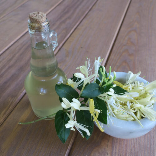 A small bottle of simple syrup on a wood table. With a small bowl of white flowers