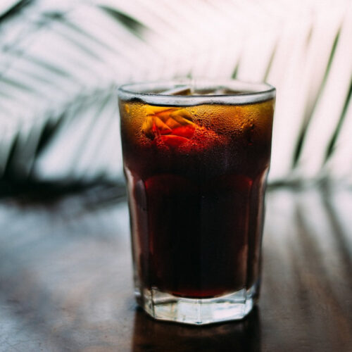 A frosty glass of iced americano coffee, standing on a dark wood table