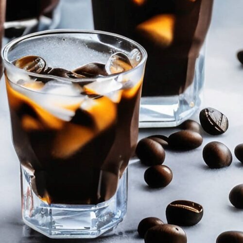 A glass of iced espresso coffee with coffee beans scattered around