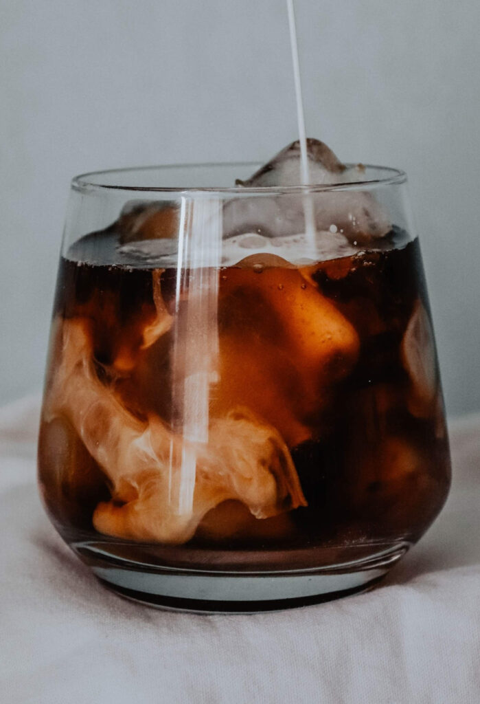 Cold milk being poured into a glass of instant cold brew coffee and ice.