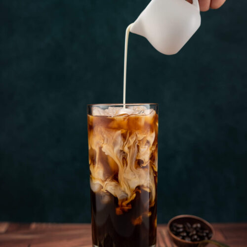 Chilled milk being poured into a glass full of iced instant coffee.