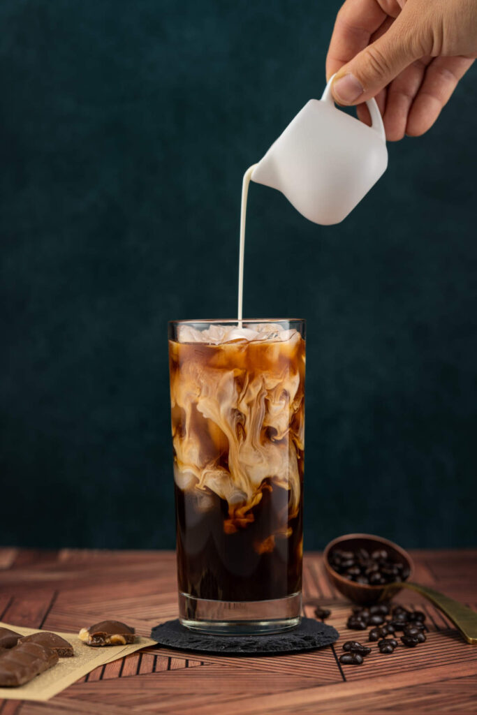 Chilled milk being poured into a glass full of iced instant coffee.