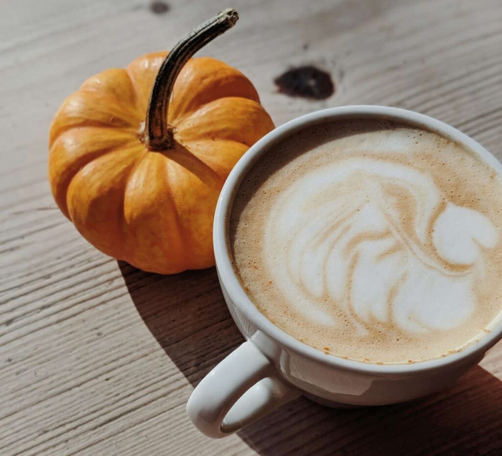 A pumpkin and a large cup of pumpkin spice latte standing on an old wooden table.