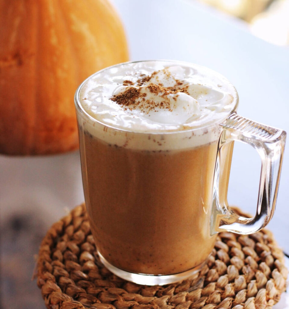 A glass mug of pumpkin spice latter topped with a sprinkle of ground cinnamon.