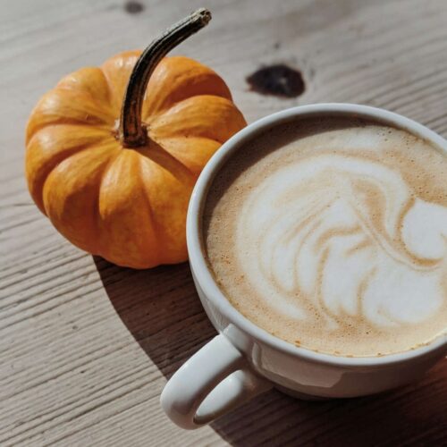 A pumpkin and a large cup of pumpkin spice latte standing on an old wooden table.