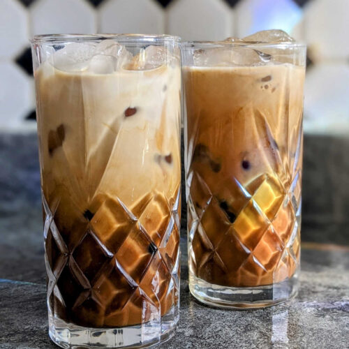 Two glassed of iced caramel macchiato on a marble worktop.