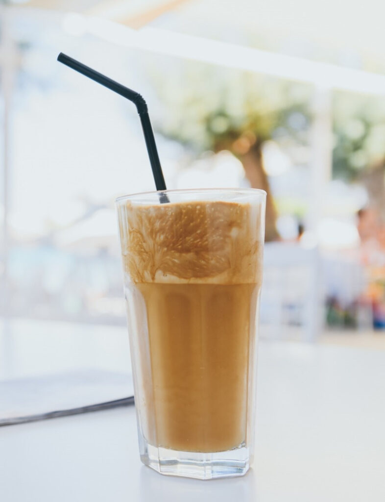 Frappe frozen coffee in a tall glass with a straw.