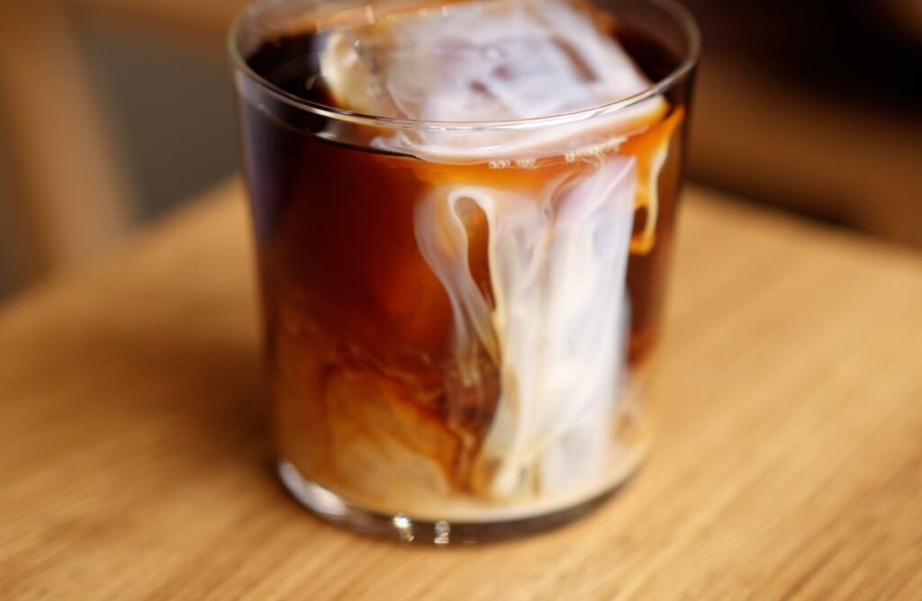 A glass of iced coffee with chilled milk being poured into it.